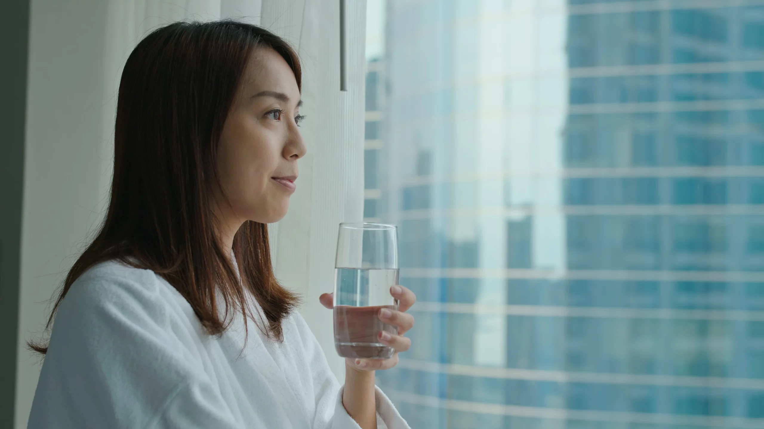 Woman looking out the window and holding glass of water.