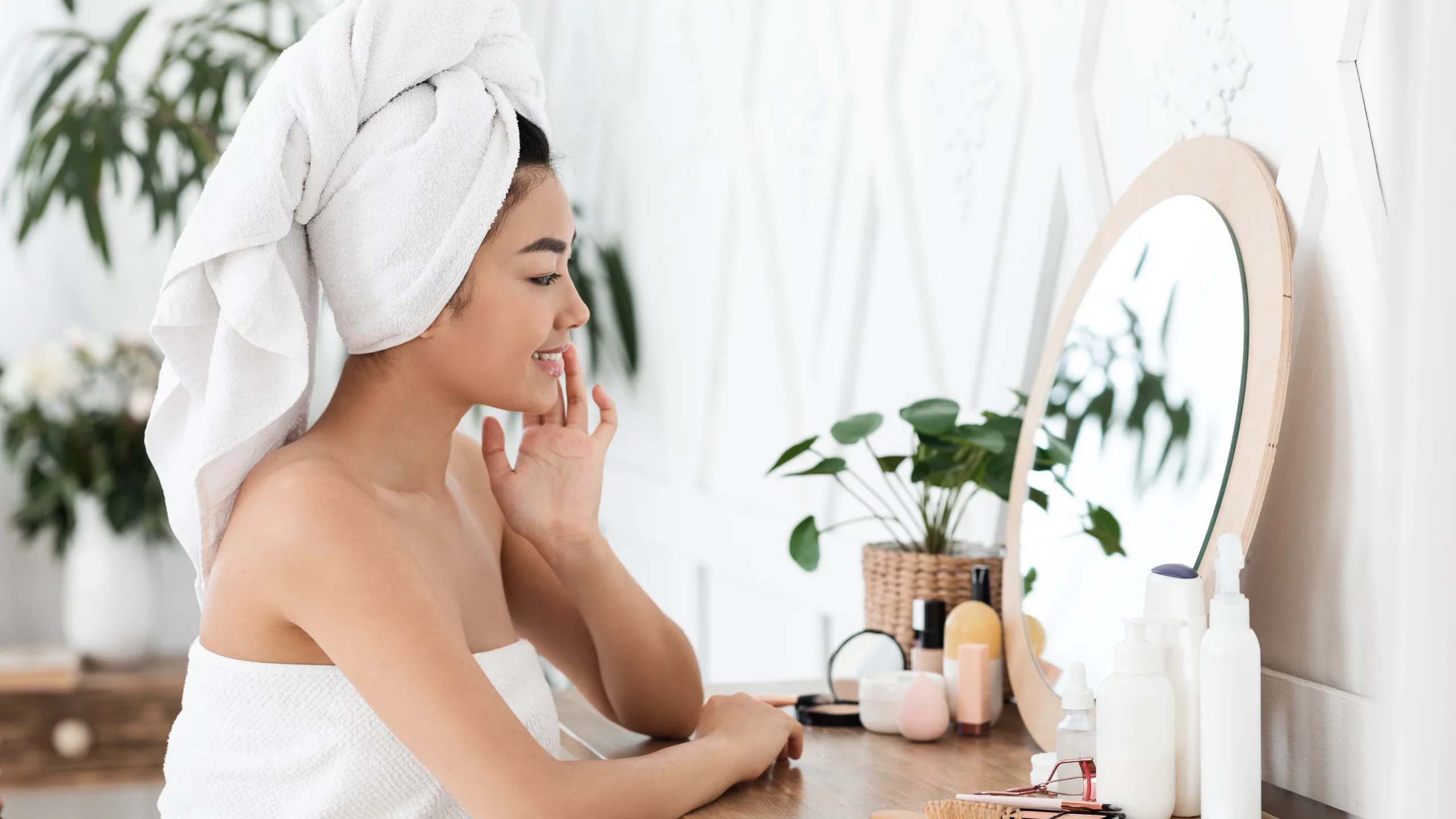 Side view of a woman wrapped in a towel and towel over her hair looking in a mirror.