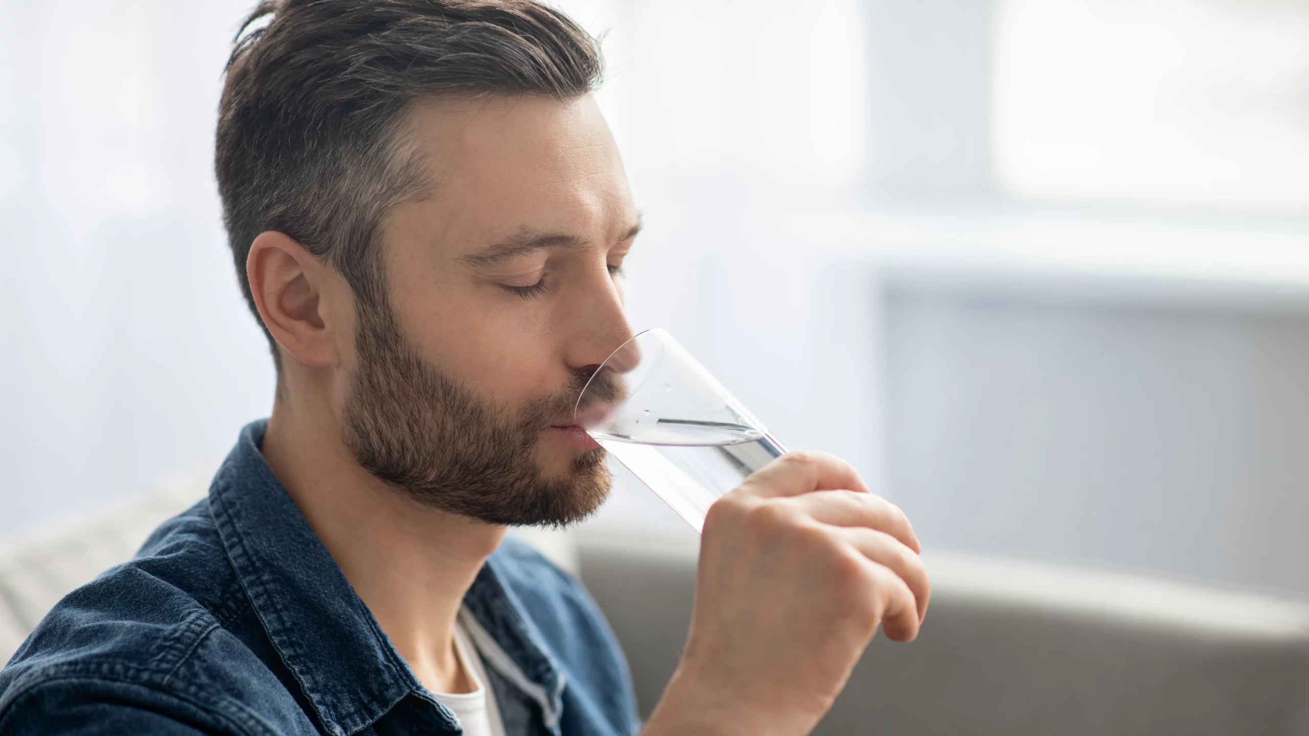 Side profile of a man with a beard drinking a glass of water.
