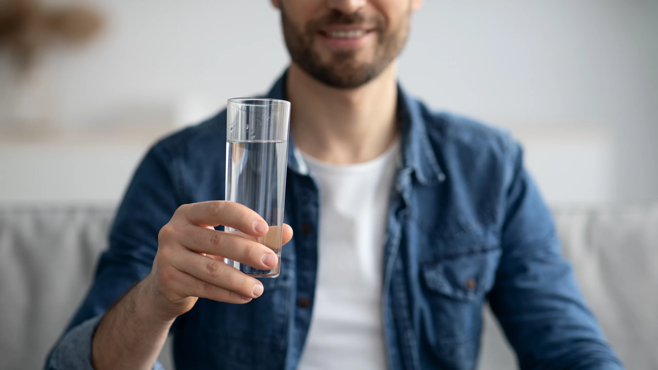 Cropped image of a man with a beard holding a glass of water.